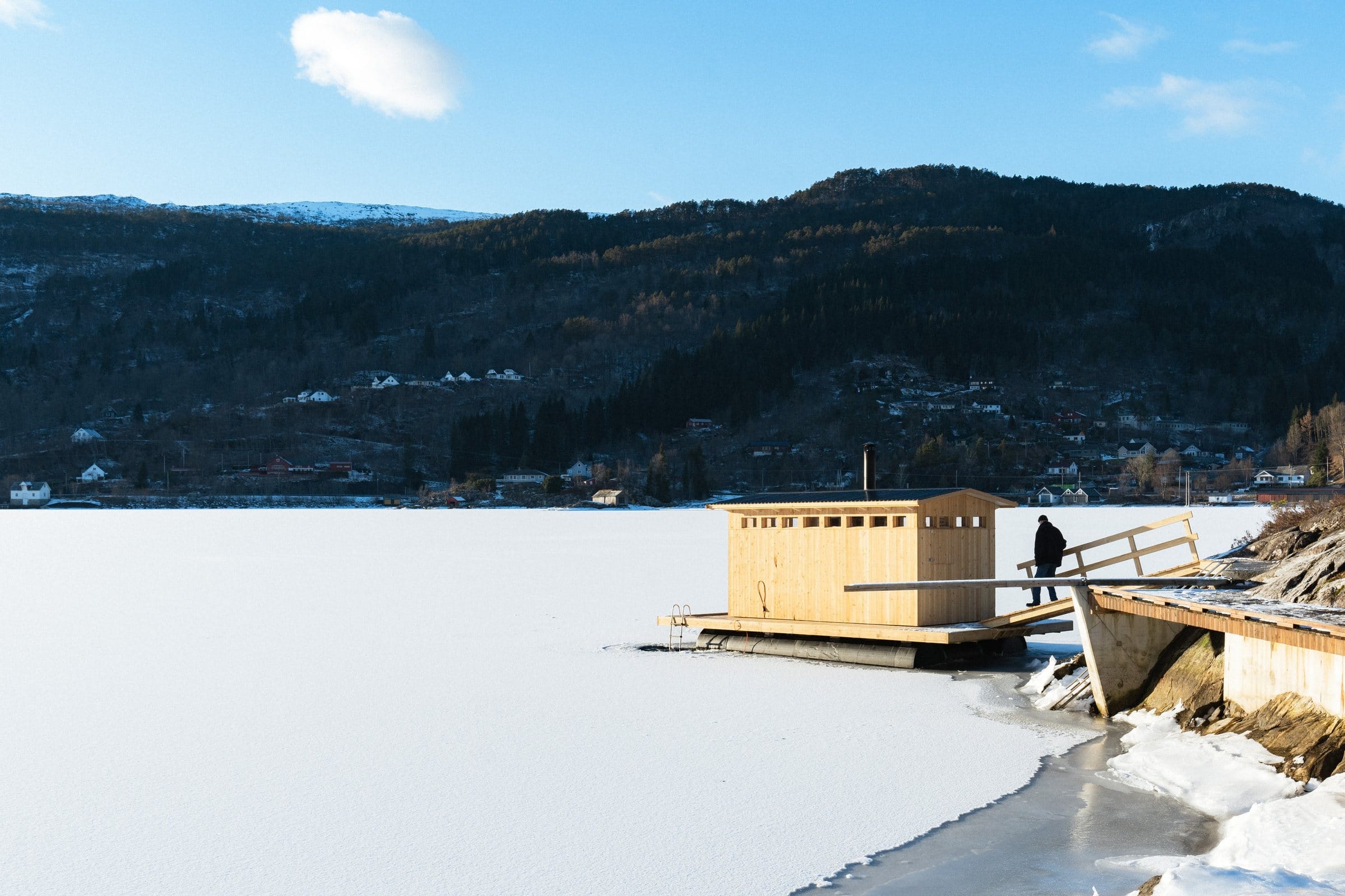 Bjørkheim Sauna out in the frozen Teigavika bay, with forest and mountains behind