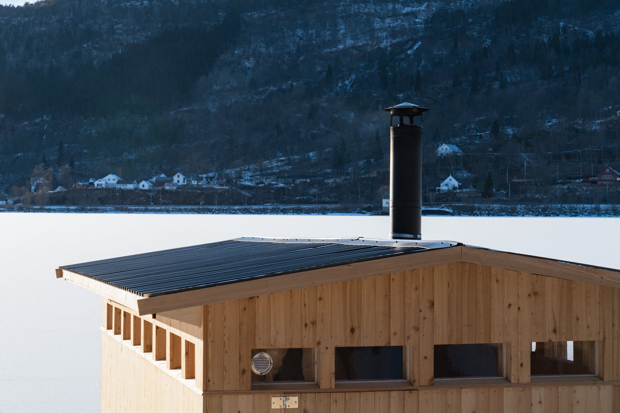 The sauna from the side, with the chimney and the fjord behind